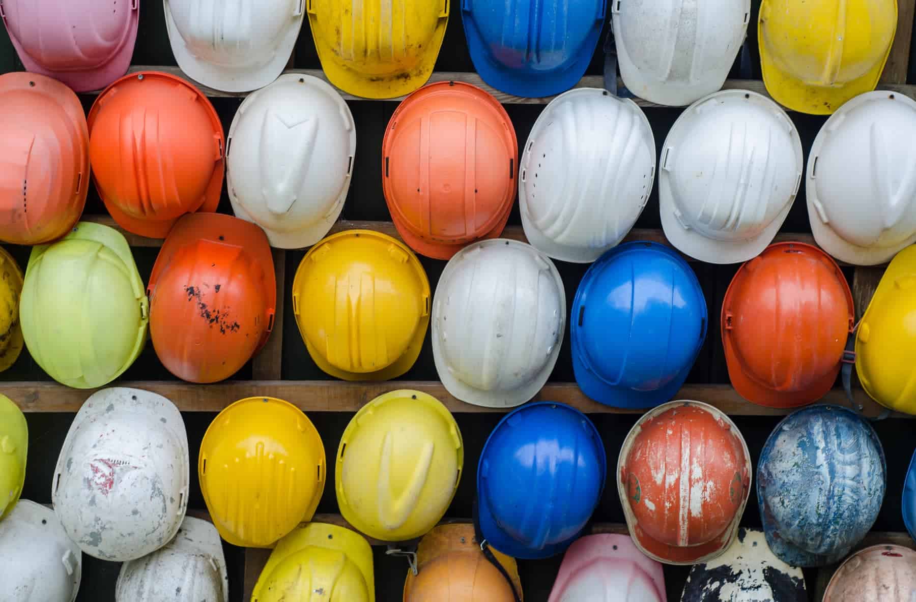 Blue, yellow, orange, and white construction hard hats lined up randomly in several rows.