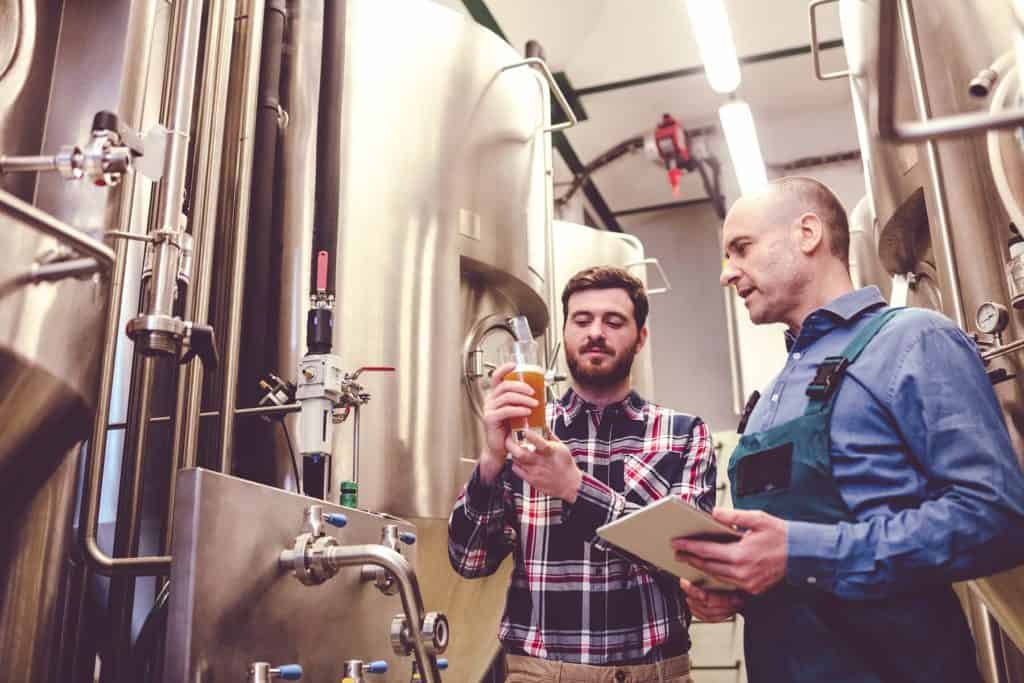 Owner of a brewery with a worker inspecting beer.