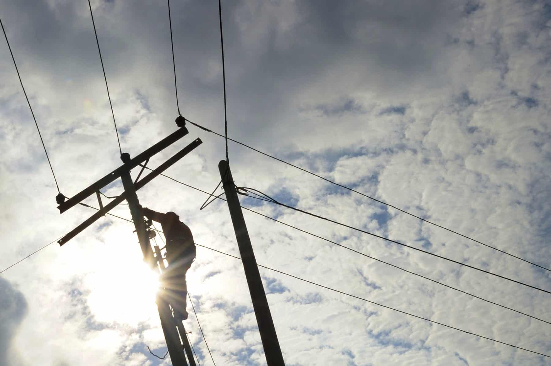 A person on a ladder working on the electrical and telephone lines.