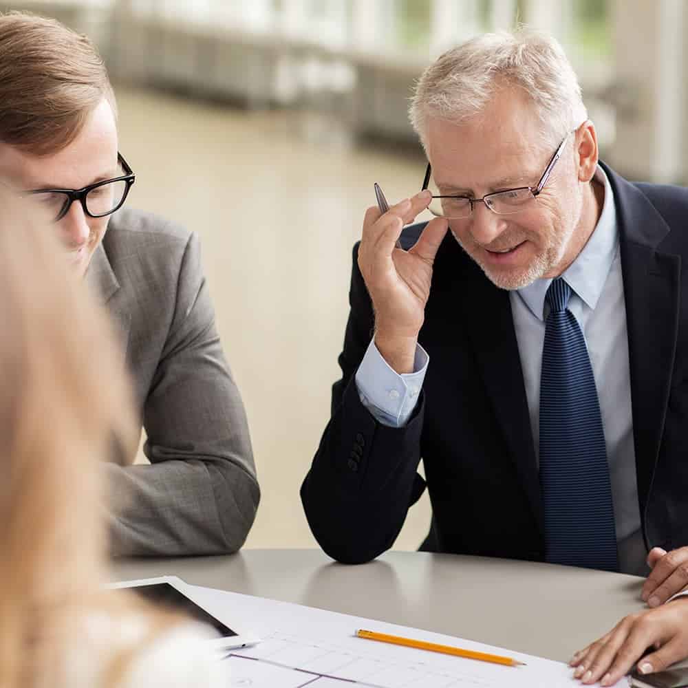 A middle aged man and a young man happily discussing construction blueprints with a PC in an office space.