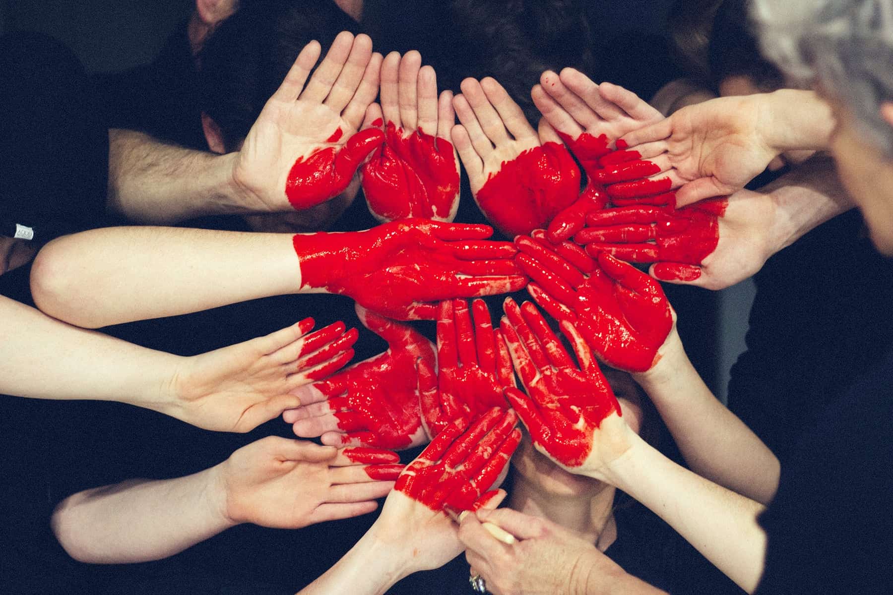 Multiple people's hands put together and painted in a red heart.