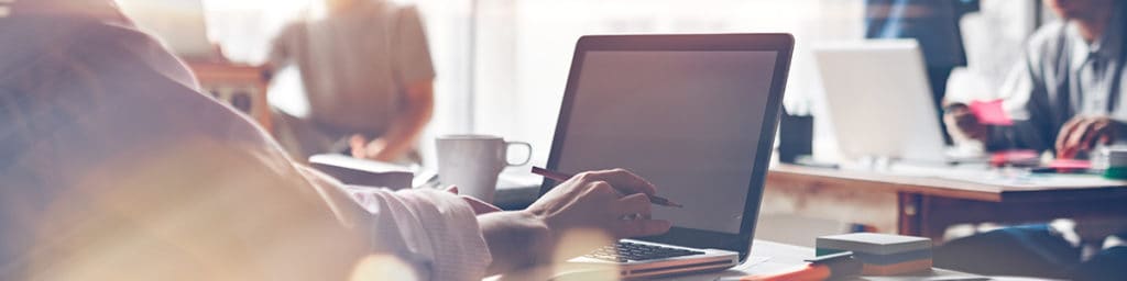 A person in an office on a laptop with others surrounding them.