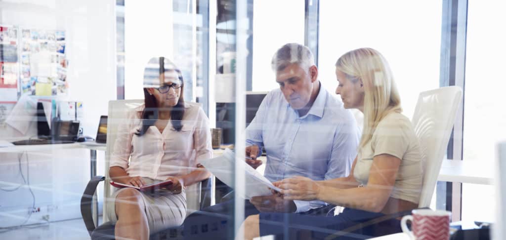 Two certified succession planners and a client in a brightly lit office working on a transition plan.