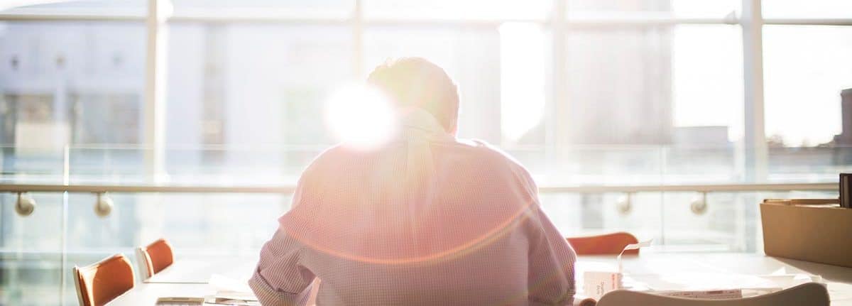 A corporate executive sitting at a table facing bright windows contemplating his executive wealth management strategies.