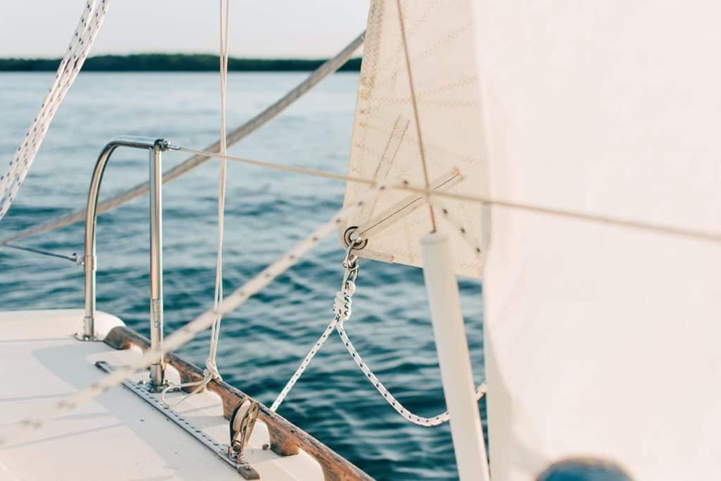 A photo looking at the bottom portion of a white sail on a boat floating on blue water.