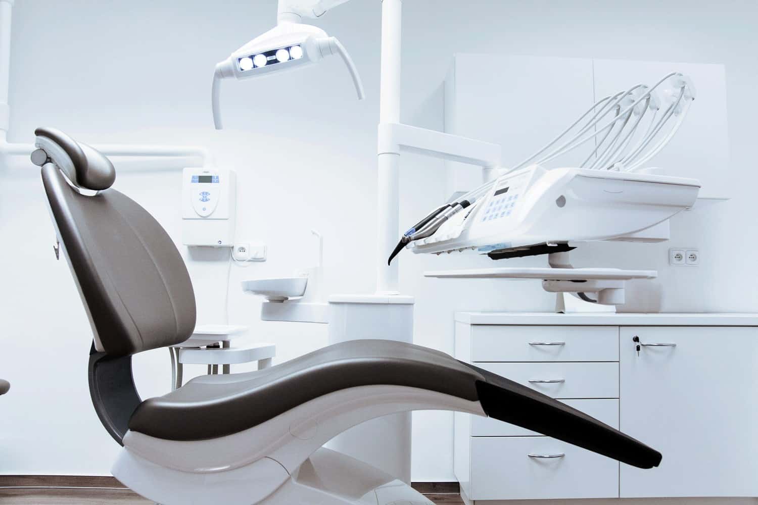 A brown dental chair surrounded by white dental equipment and cabinets in a dental office. Dentists should look to dental CPAs to help them grow their practice during the COVID-19 pandemic.