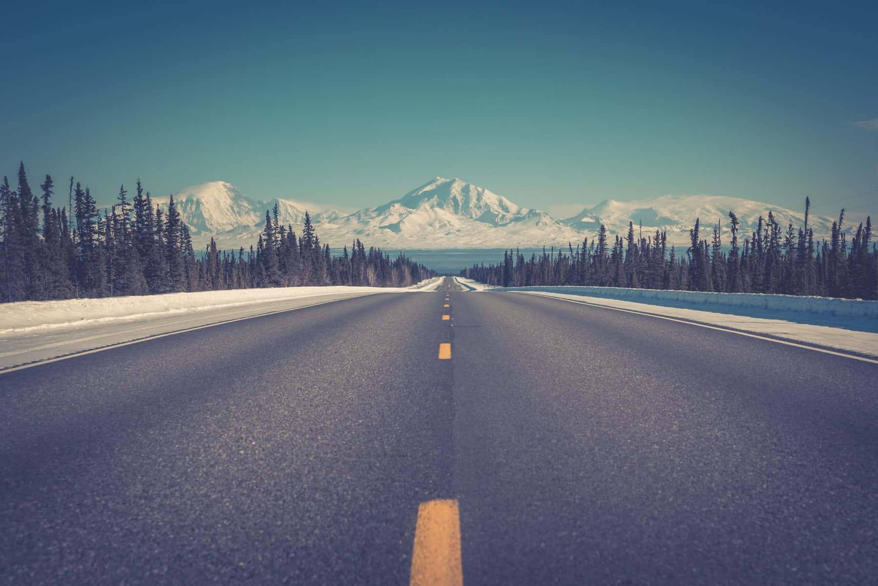 A view from the middle of a road showing the snowy mountains and trees of Alaska, where Aldrich Advisors announces new personnel moves in their Alaska-based consulting team, specializing in utilities.