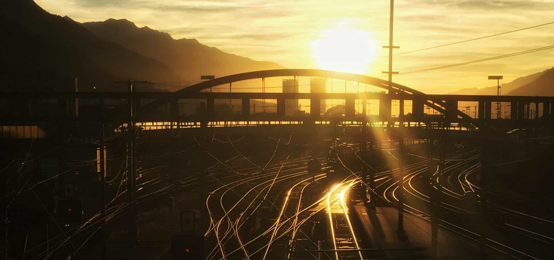 Sunset view of a railroad in an industrial area with a bridge off in the distance