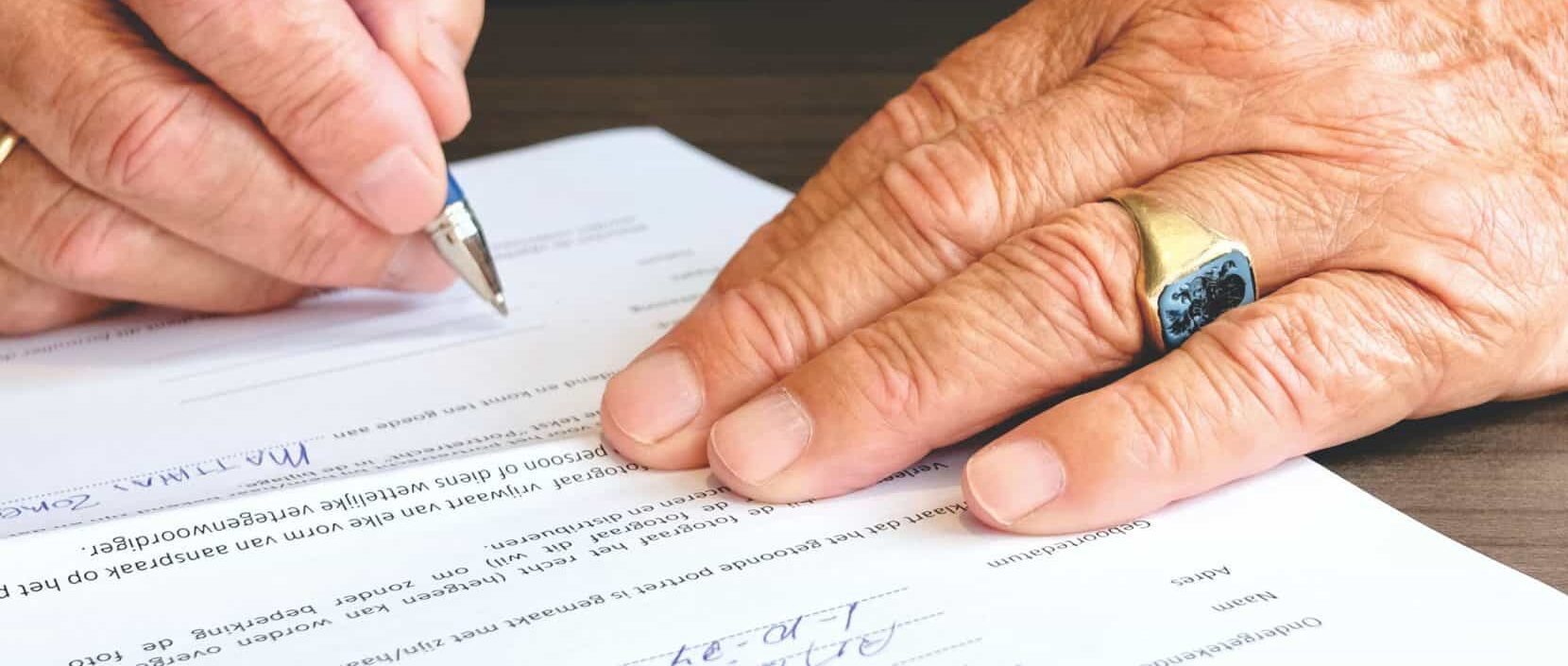 person signing paperwork by hand with blue pen