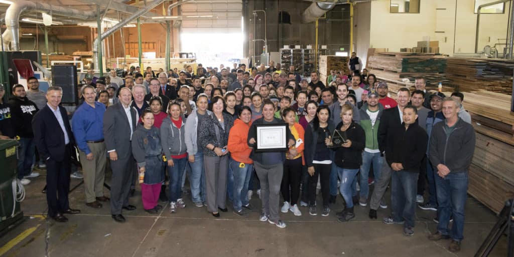 Crowd of employees standing in a warehouse while one in front holds an award