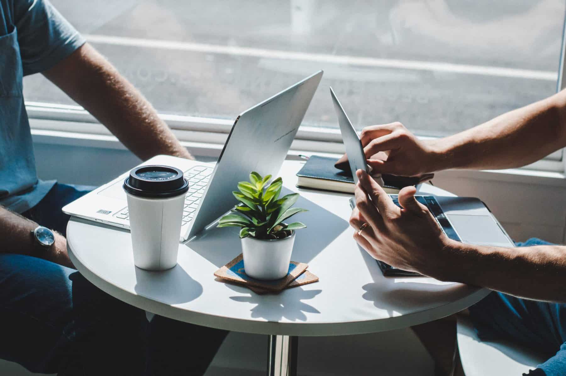 Two businessmen sit at a cafe table with a small plant to discuss M&A Activity in Q2 2022