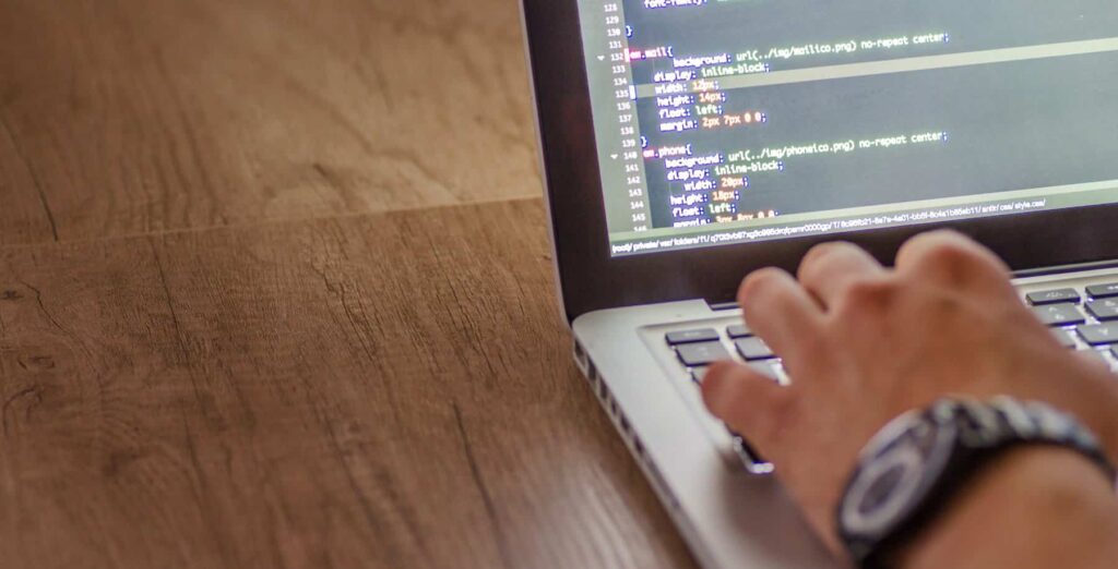 cybersecurity professional review code on a silver laptop sitting on a wooden desk