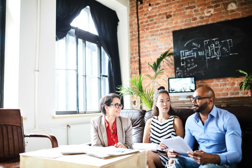 Three nonprofit leaders sit in a room with a brick accent wall and discuss donor acquisition strategies