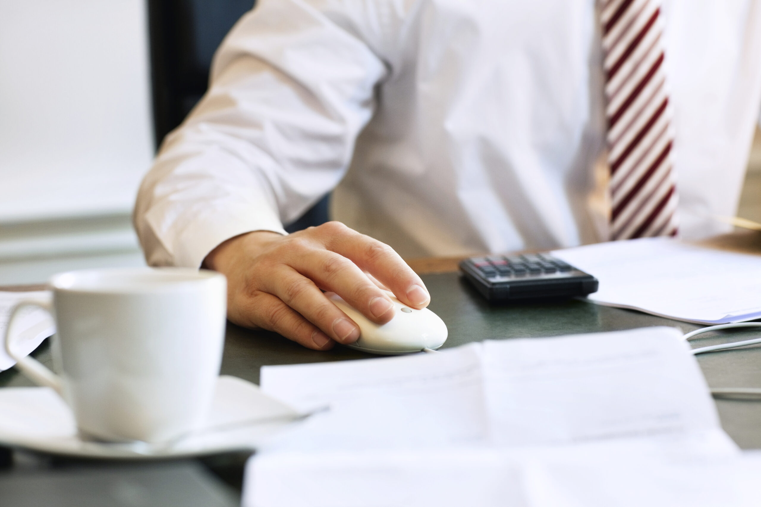 Businessman using computer mouse at work, cup and saucer in the foreground