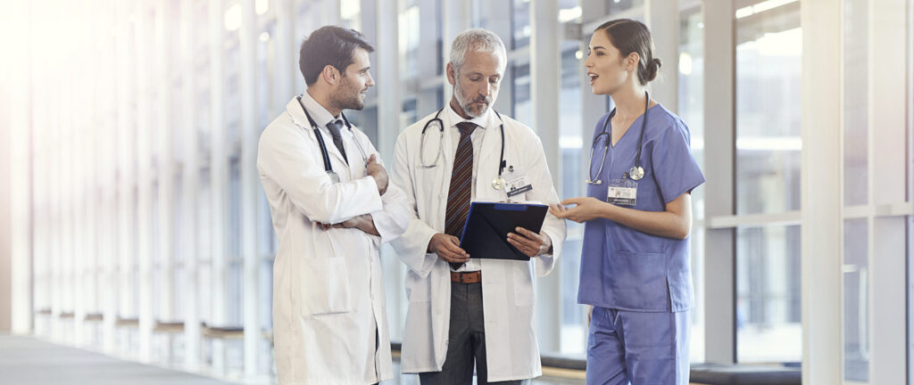 three healthcare employees standing in a hall with large bright windows, discussing employee fringe benefits