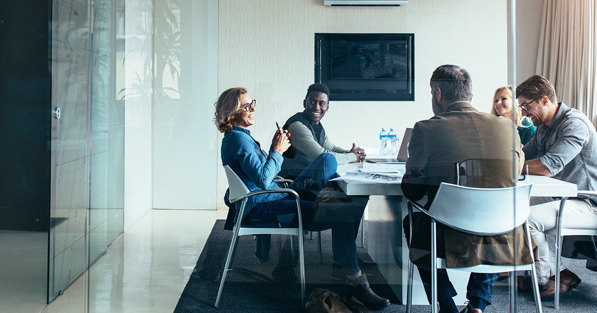 Four people sitting around a square table in a modern, bright meeting room.