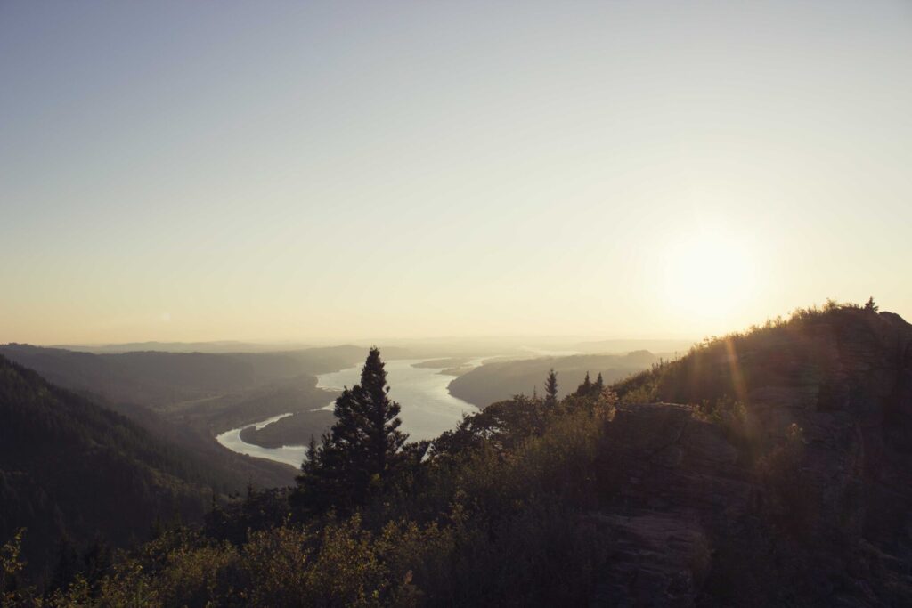 Overlooking tree covered hills with a wide river in the distance at dusk.