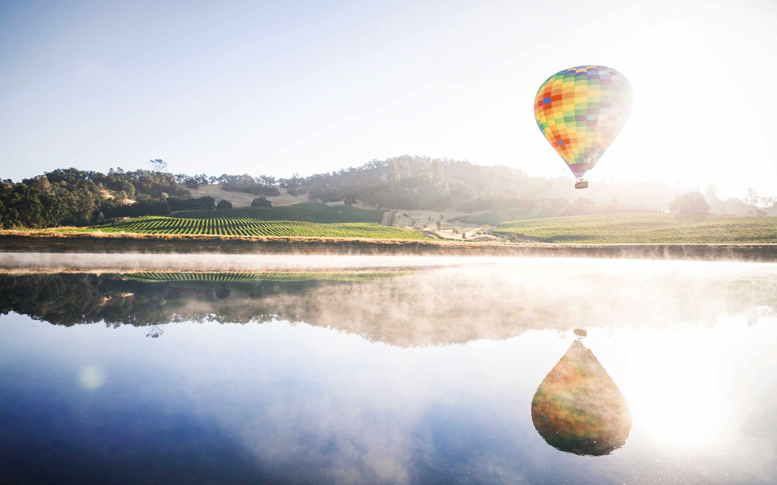 hot air balloon over a glassy lake with mountain in the background